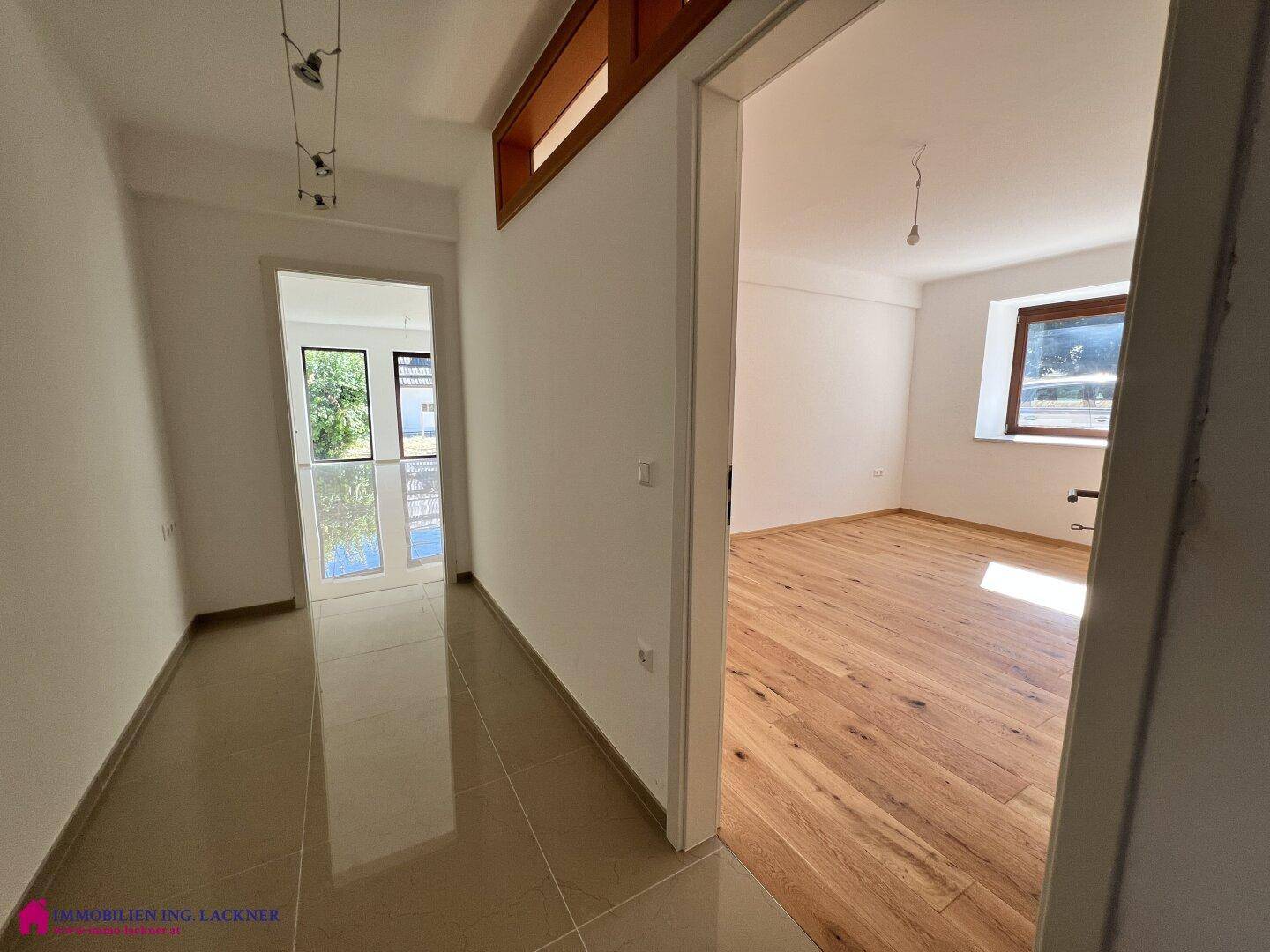 Heller Flur mit Fliesenboden, der zu einem Zimmer mit Holzparkett führt.