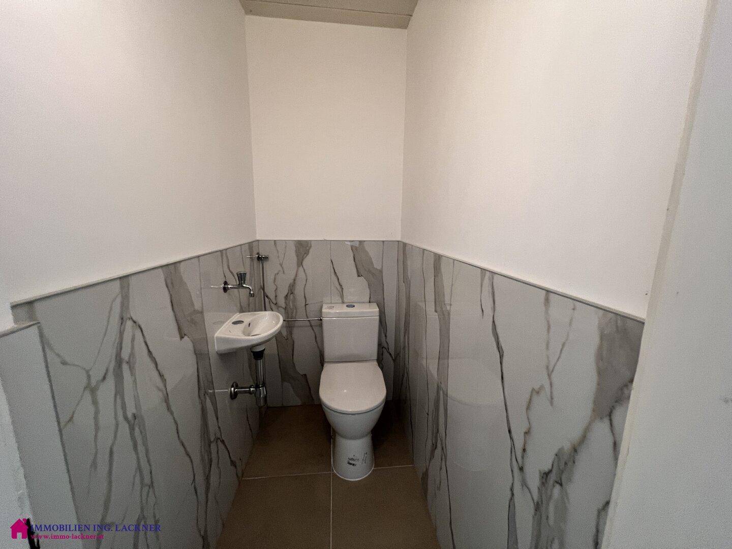 Separates WC mit Wand-WC, kleinem Waschbecken und modernen Marmorfliesen.