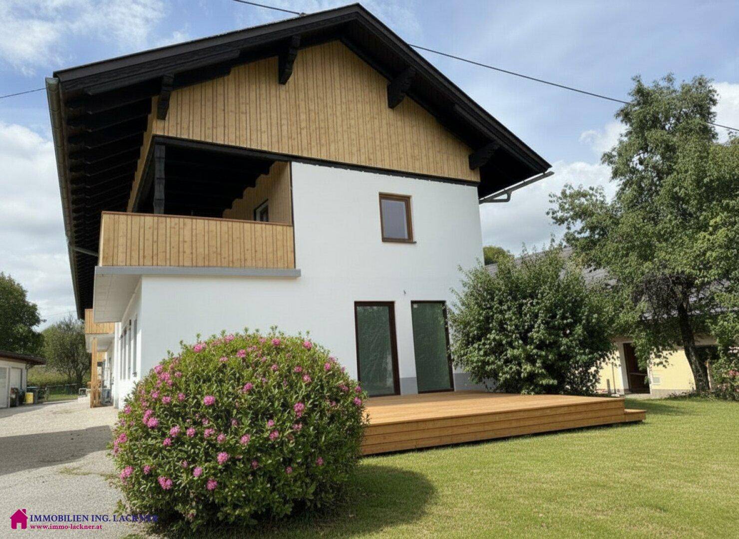 Attraktives Haus mit Holzfassade, großer Holzterrasse und gepflegtem Gartenbereich.