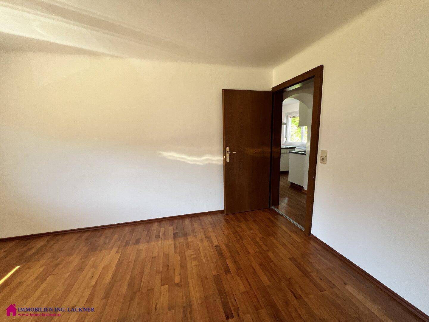 Geräumiges Zimmer mit Laminatboden und weißen Wänden, mit Zugang zu einem angrenzenden Raum.