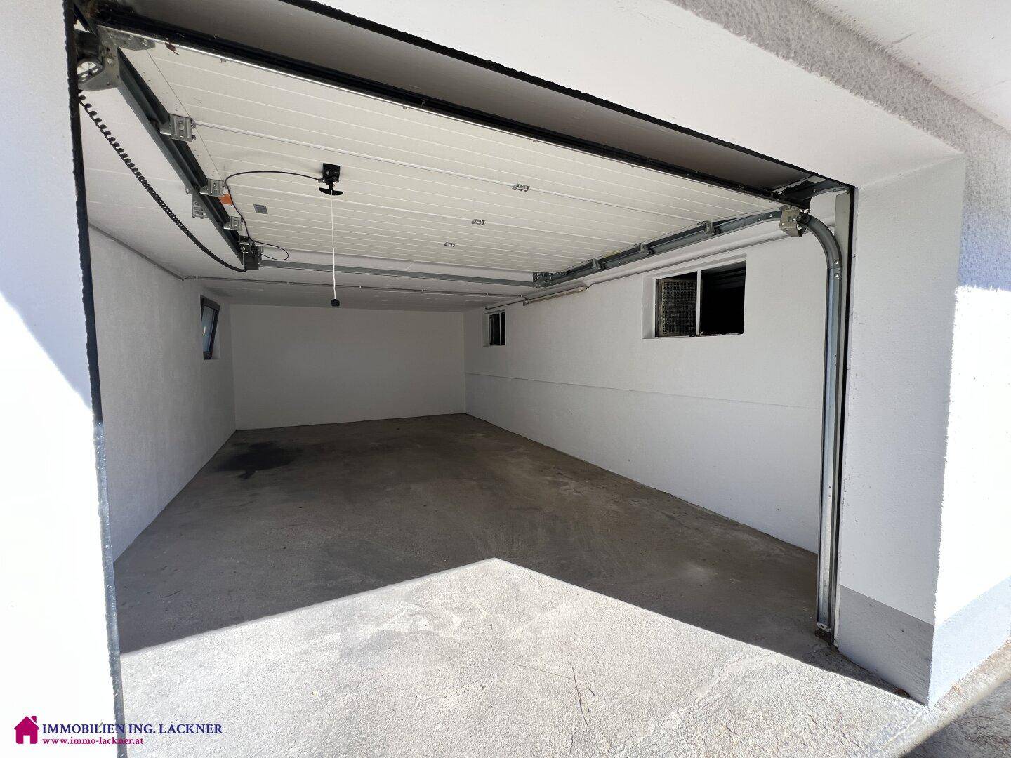 Geräumige Garage mit automatischem Tor, Betonboden und kleinen Fenstern für Belüftung.