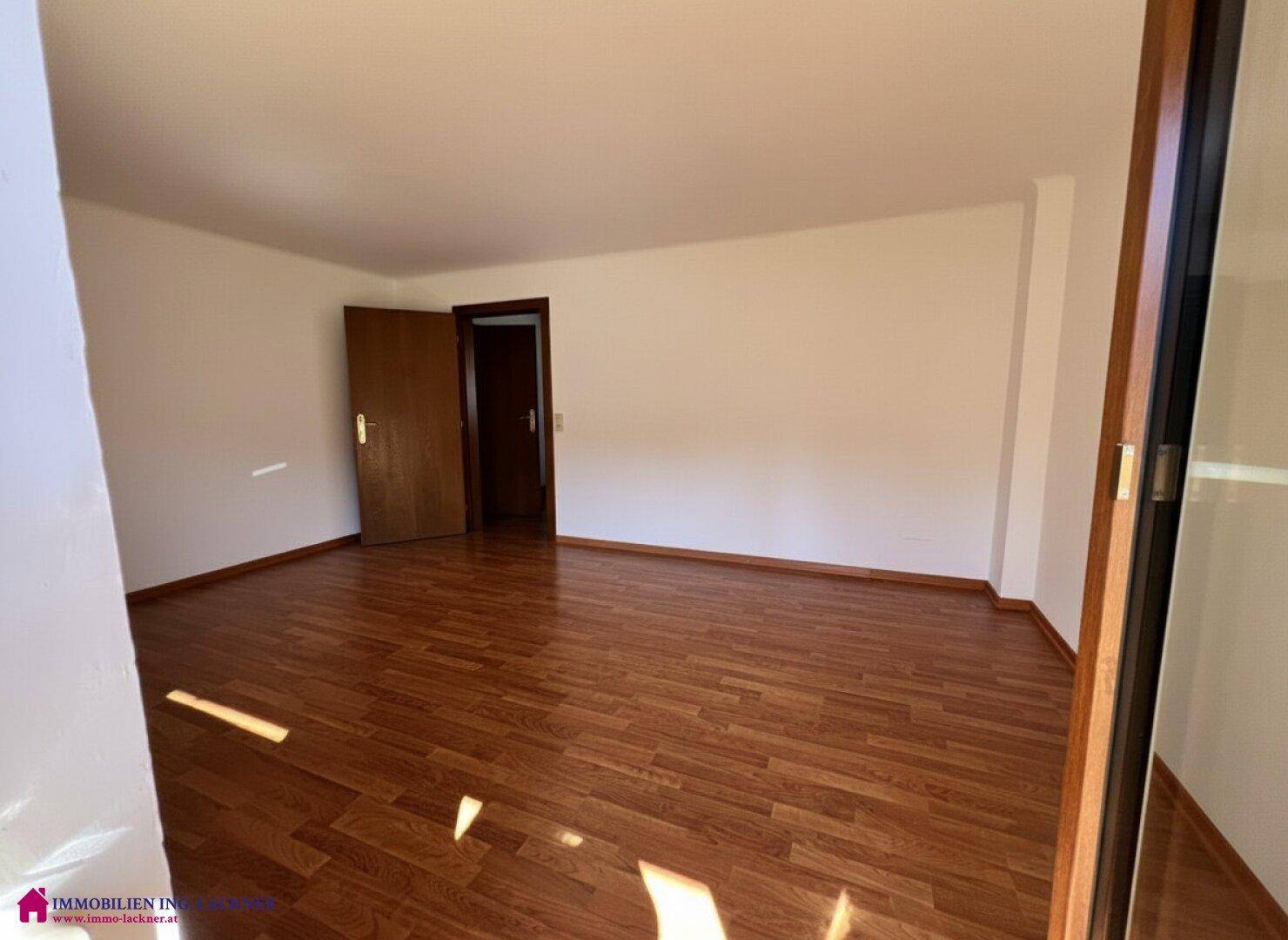 Helles Schlafzimmer mit Laminatboden und weißen Wänden, durchflutet von natürlichem Sonnenlicht.