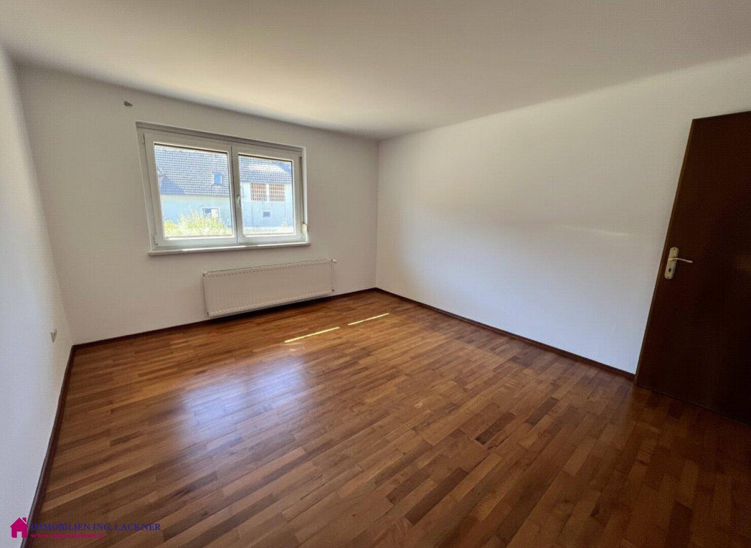 Leeres Zimmer mit Laminatboden und weißen Wänden, mit Fenster für natürliches Licht.