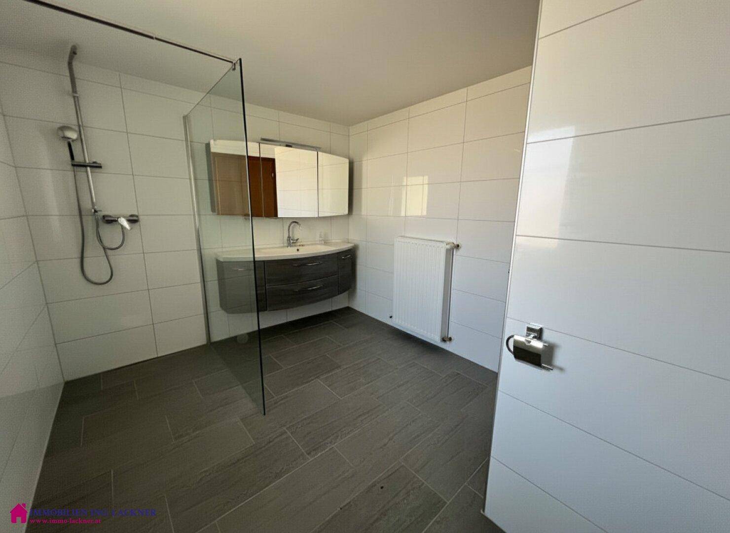 Modernes Badezimmer mit weißen Wandfliesen, grauen Bodenfliesen und einer begehbaren Dusche.