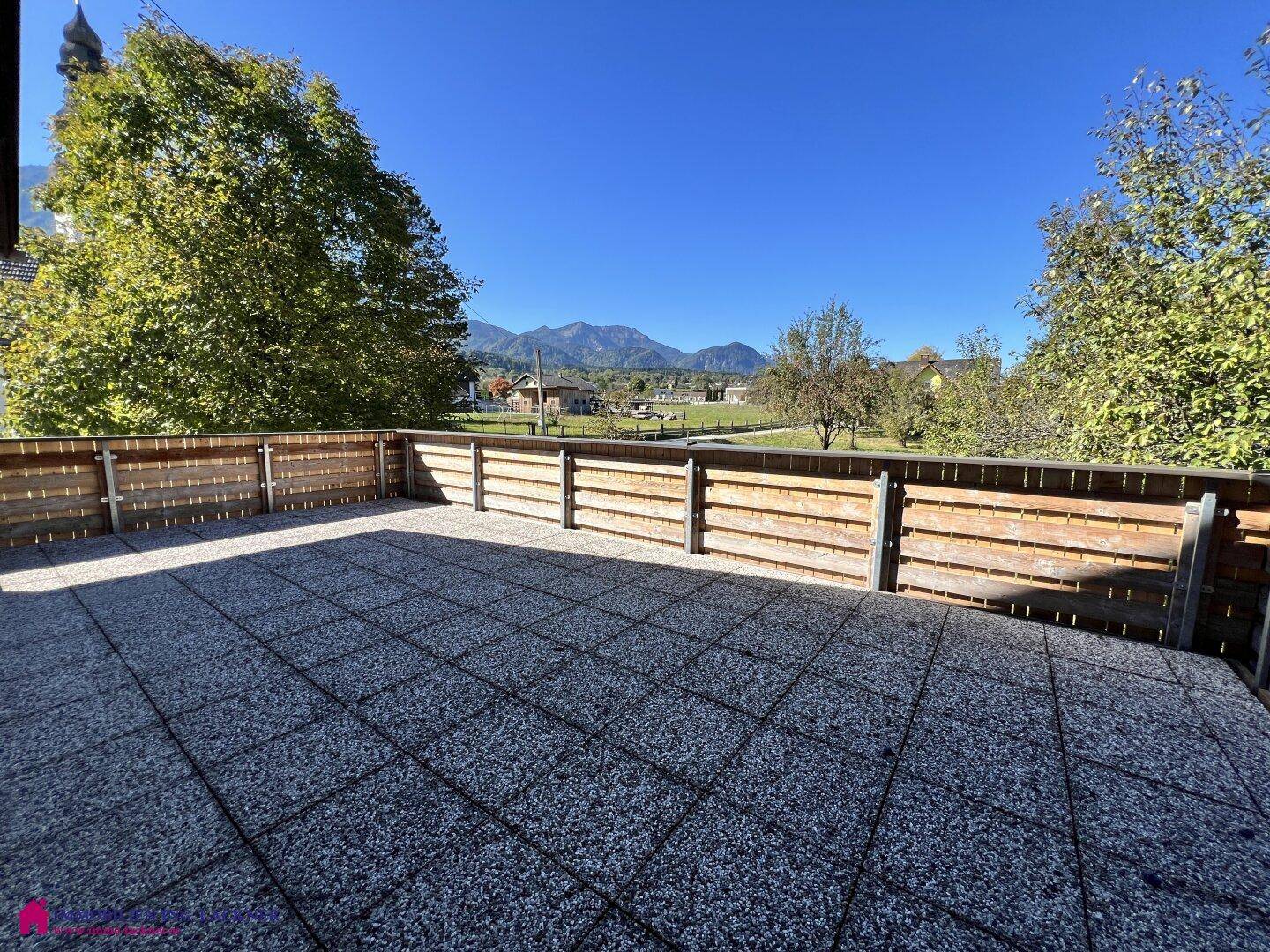 Weitläufige Terrasse mit grauen Fliesen und Holzzaun, bietet einen weiten Blick auf die Berge.