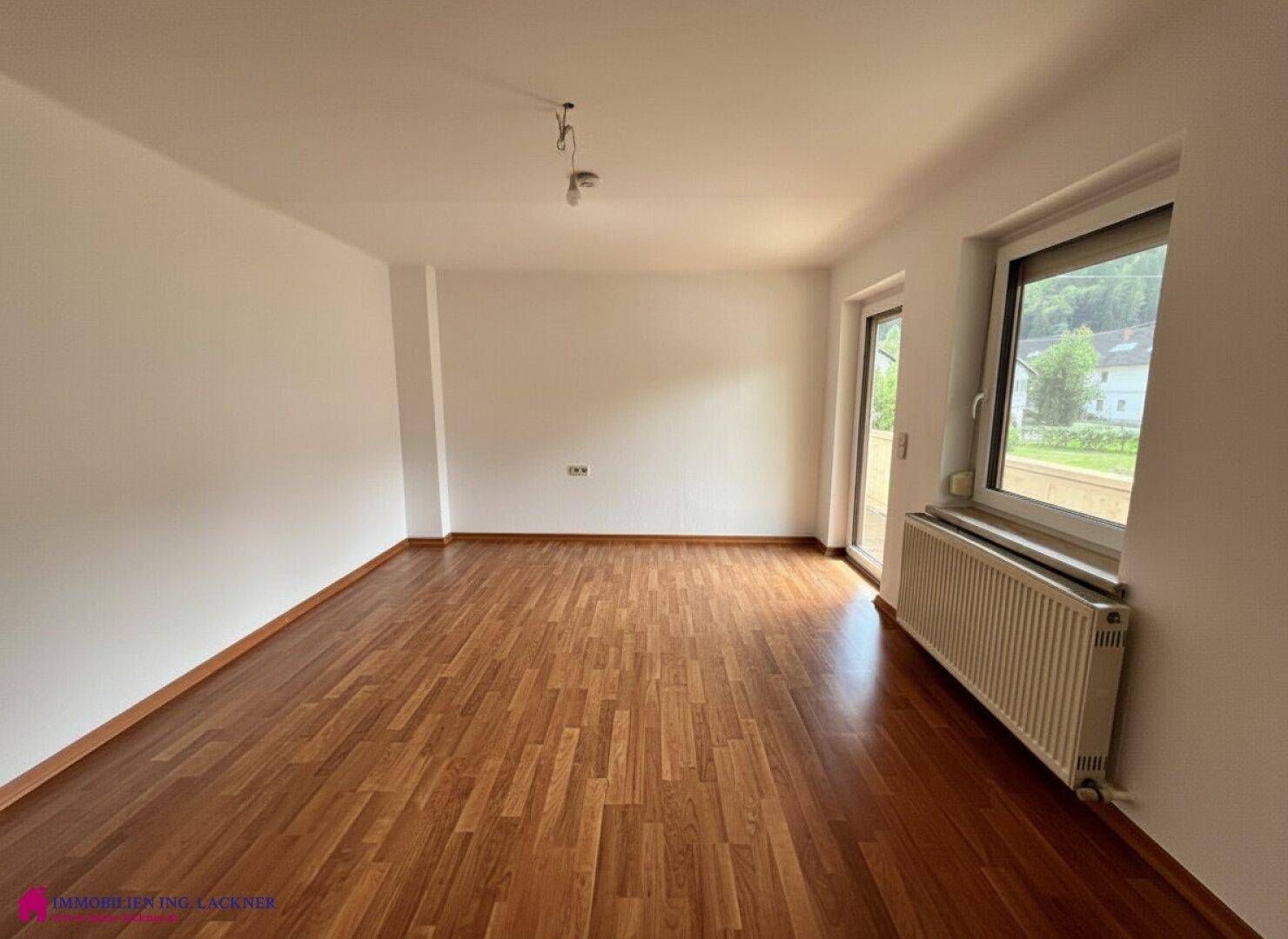 Heller Raum mit Laminatboden, weißen Wänden und Zugang zu einem Außenbereich.