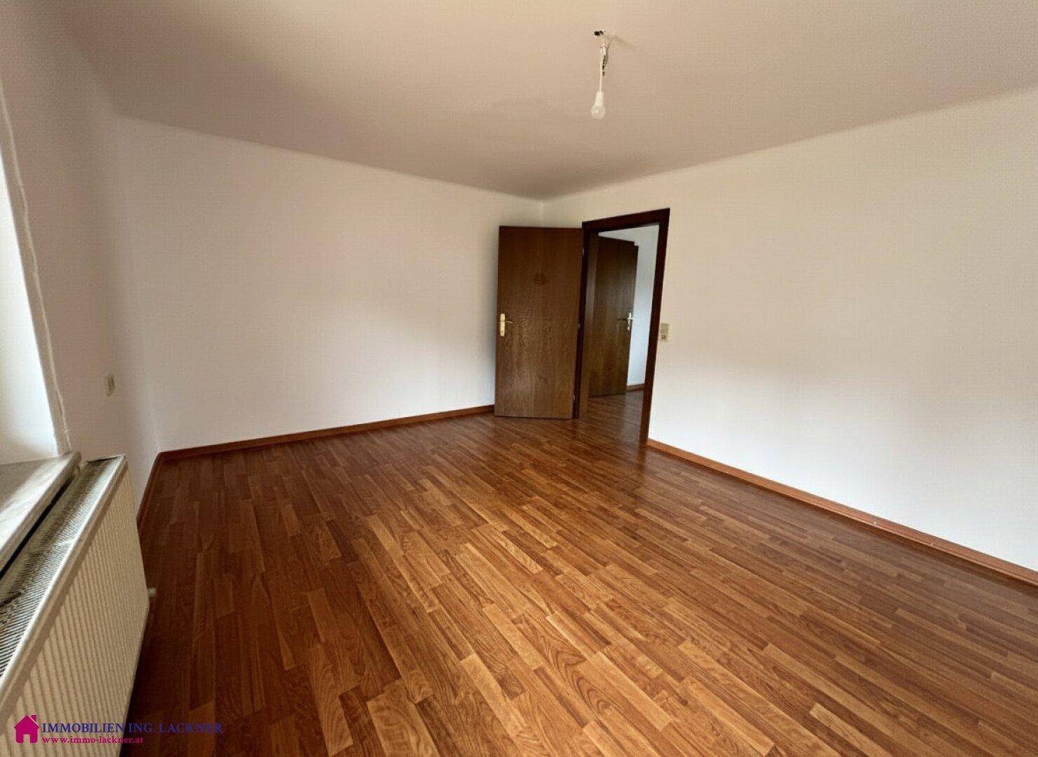 Leeres Zimmer mit Laminatboden und weißen Wänden, bereit zur individuellen Gestaltung.