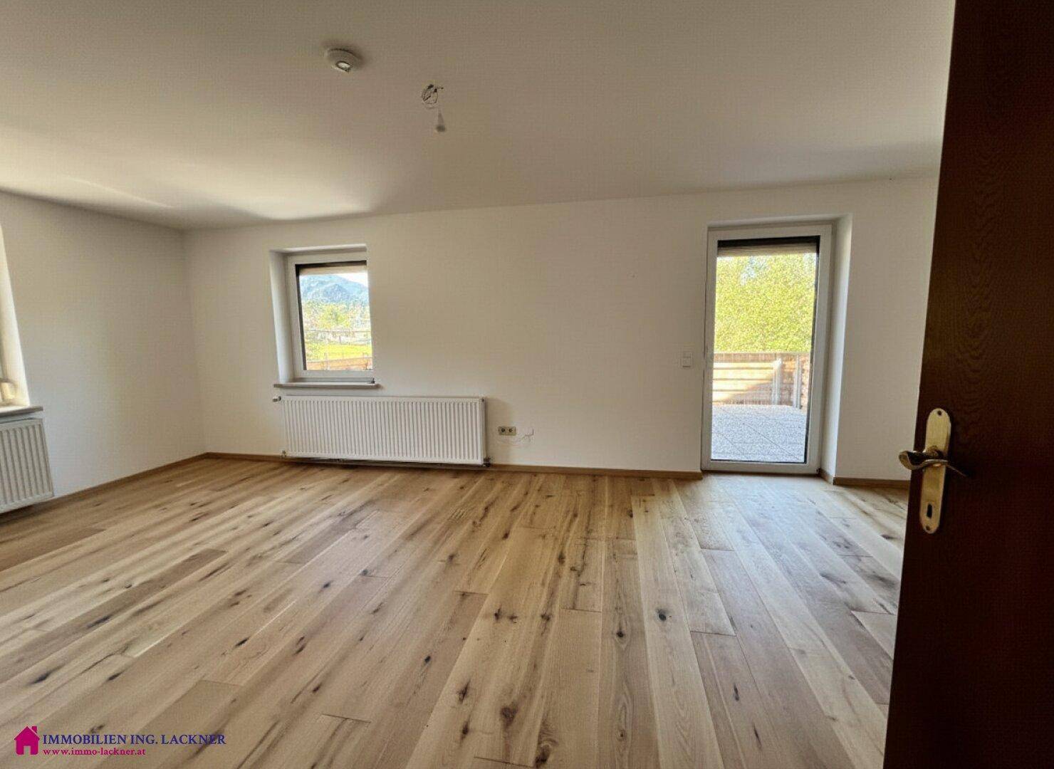 Heller Raum mit hellem Holzplankenboden, weißen Wänden und Zugang zu einem Außenbereich.