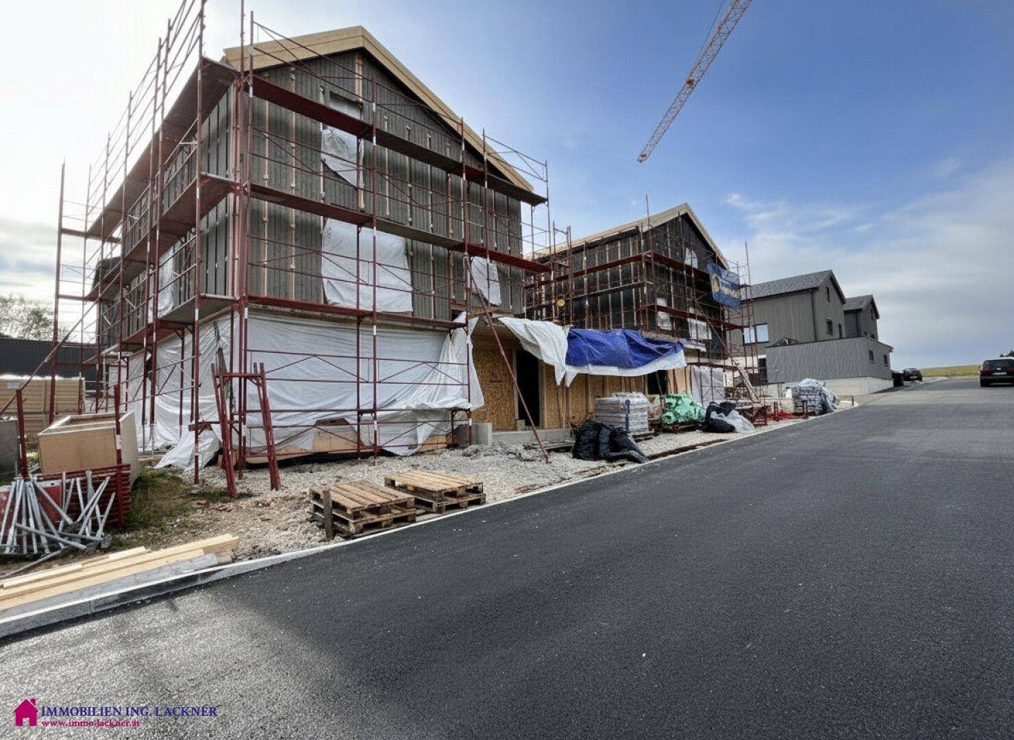 Mehrere Neubau-Doppelhaushälften in fortgeschrittener Bauphase mit Gerüsten.