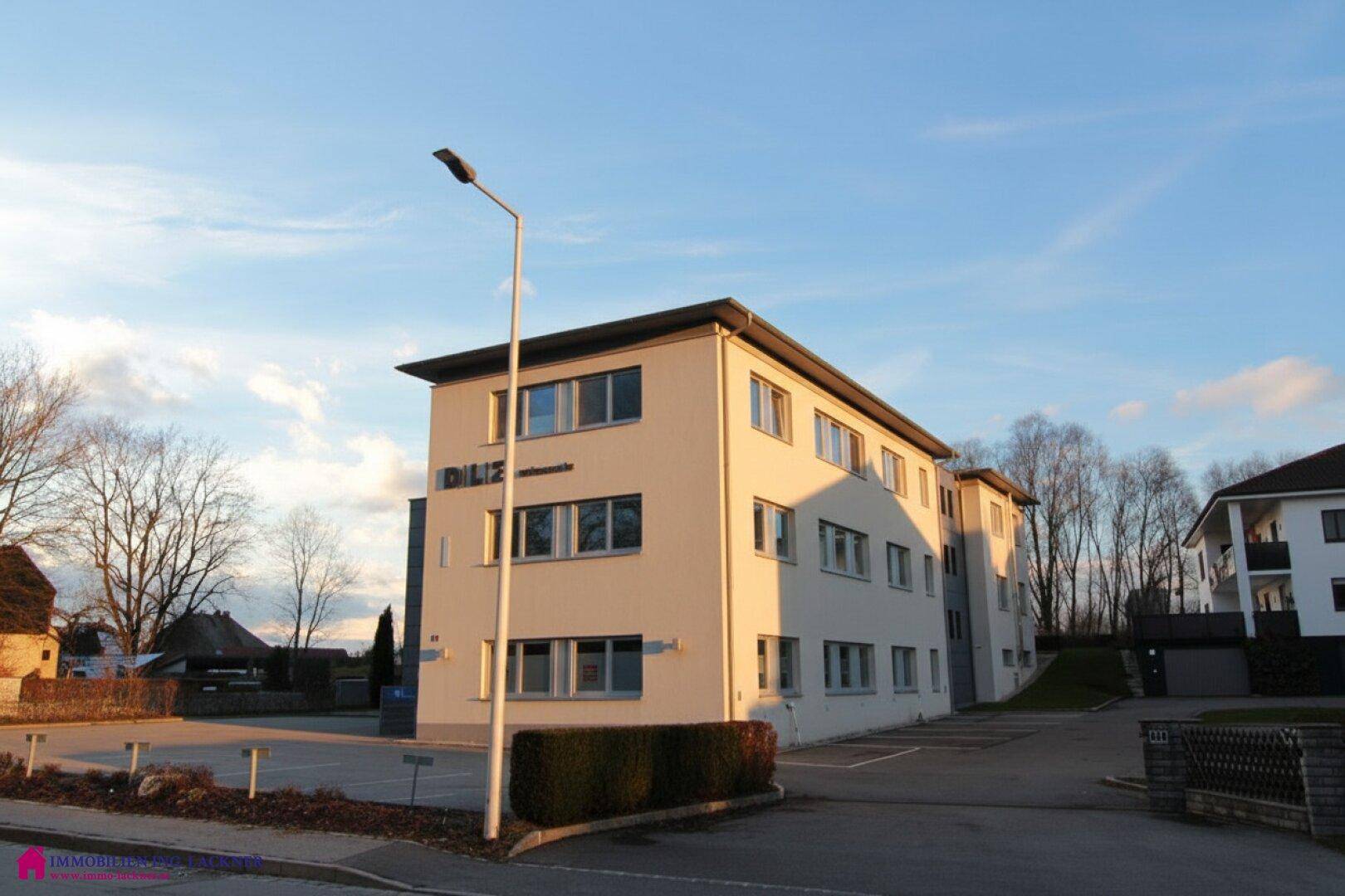 Seitenansicht des modernen Geschäftsgebäudes mit vielen Fenstern und umliegender Grünfläche.