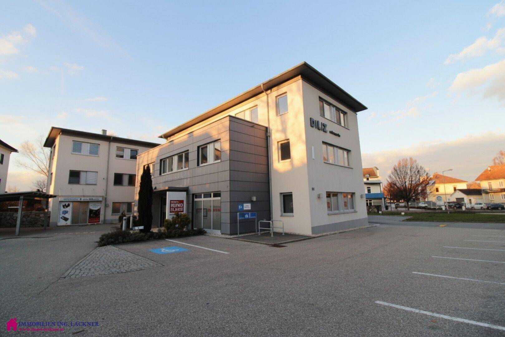 Modernes Geschäftsgebäude mit großem Parkplatz und klarem Himmel bei Sonnenuntergang.