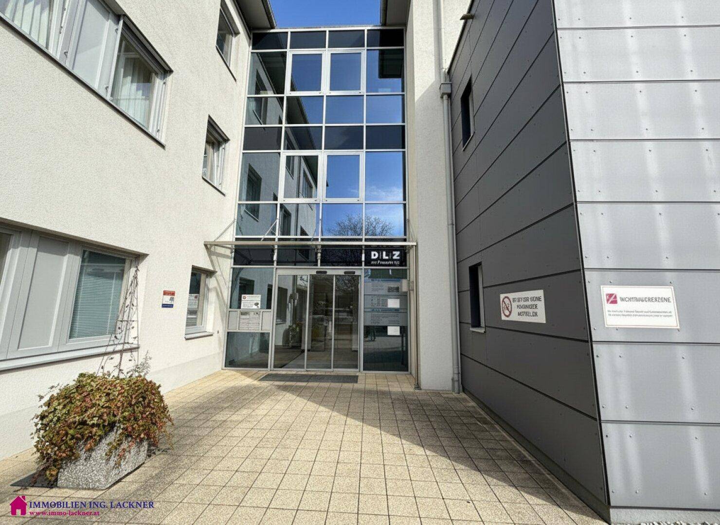 Moderner Haupteingang des Geschäftsgebäudes mit großer Glasfassade und gepflastertem Vorplatz.