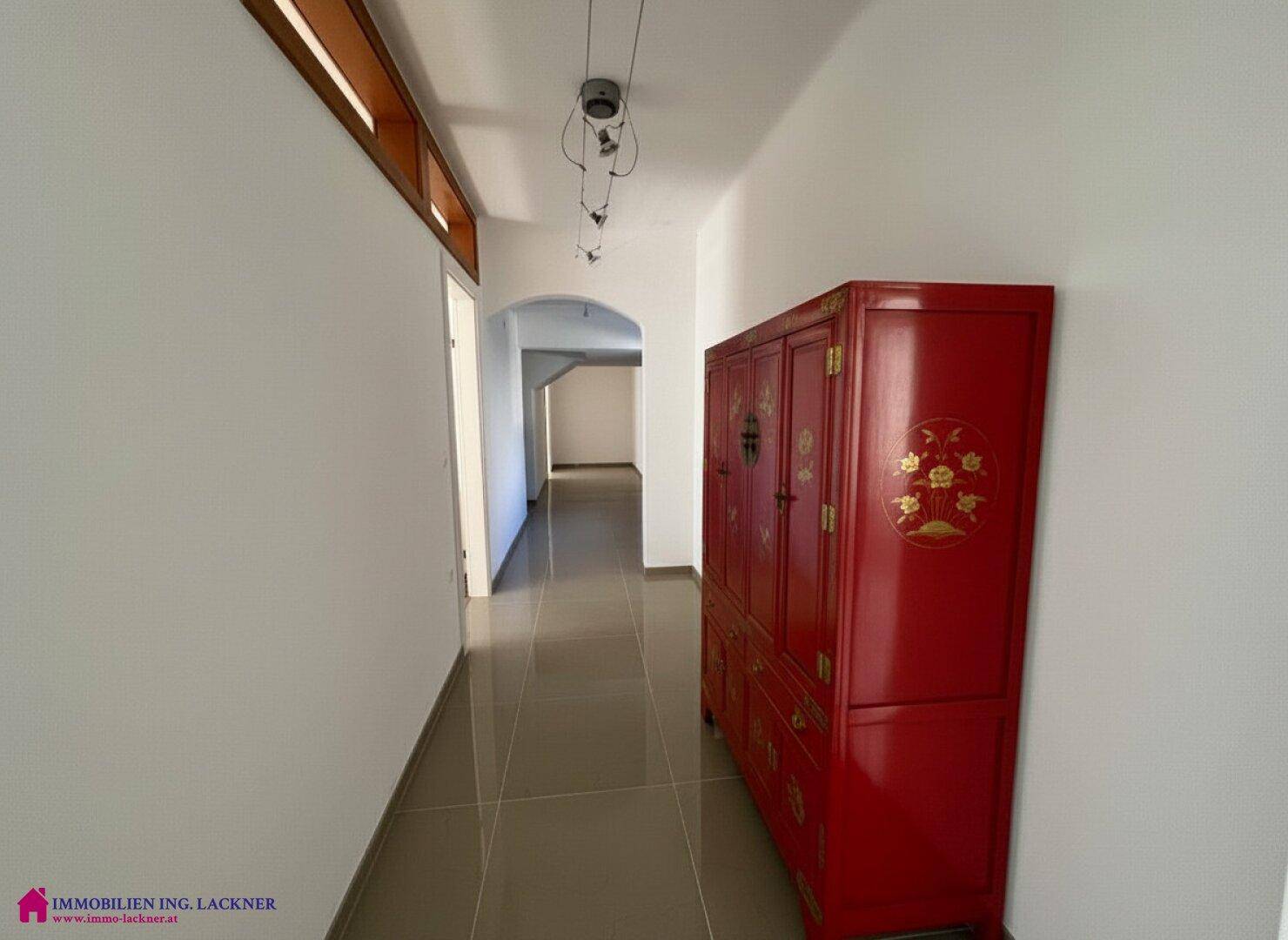 Heller Flur mit glänzenden Fliesen und einem auffälligen roten Schrank, der in einen weiteren Bereich führt.