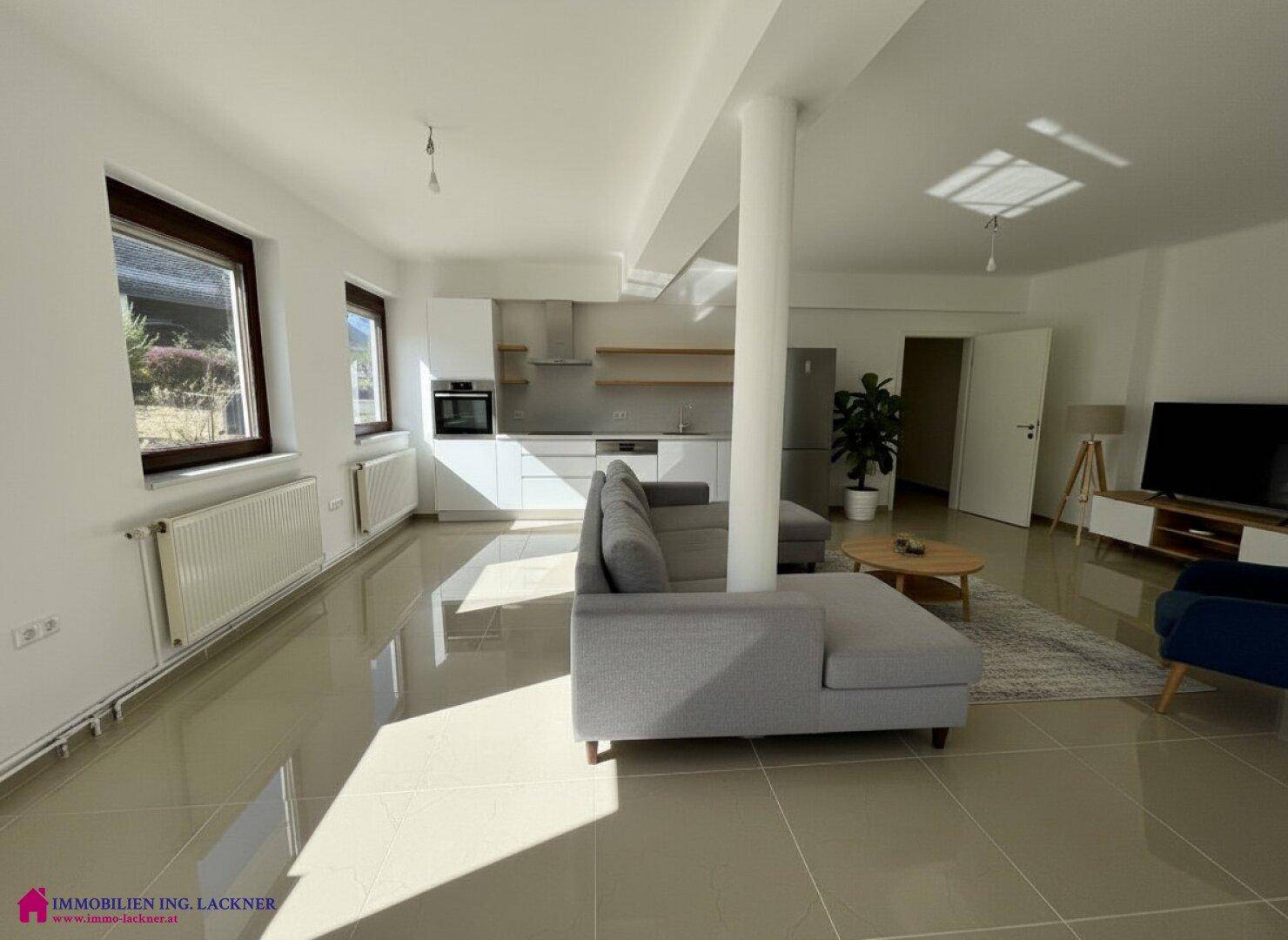 Helles, offenes Wohnzimmer mit integrierter Küche, modernen Fliesen und großem Sofa.