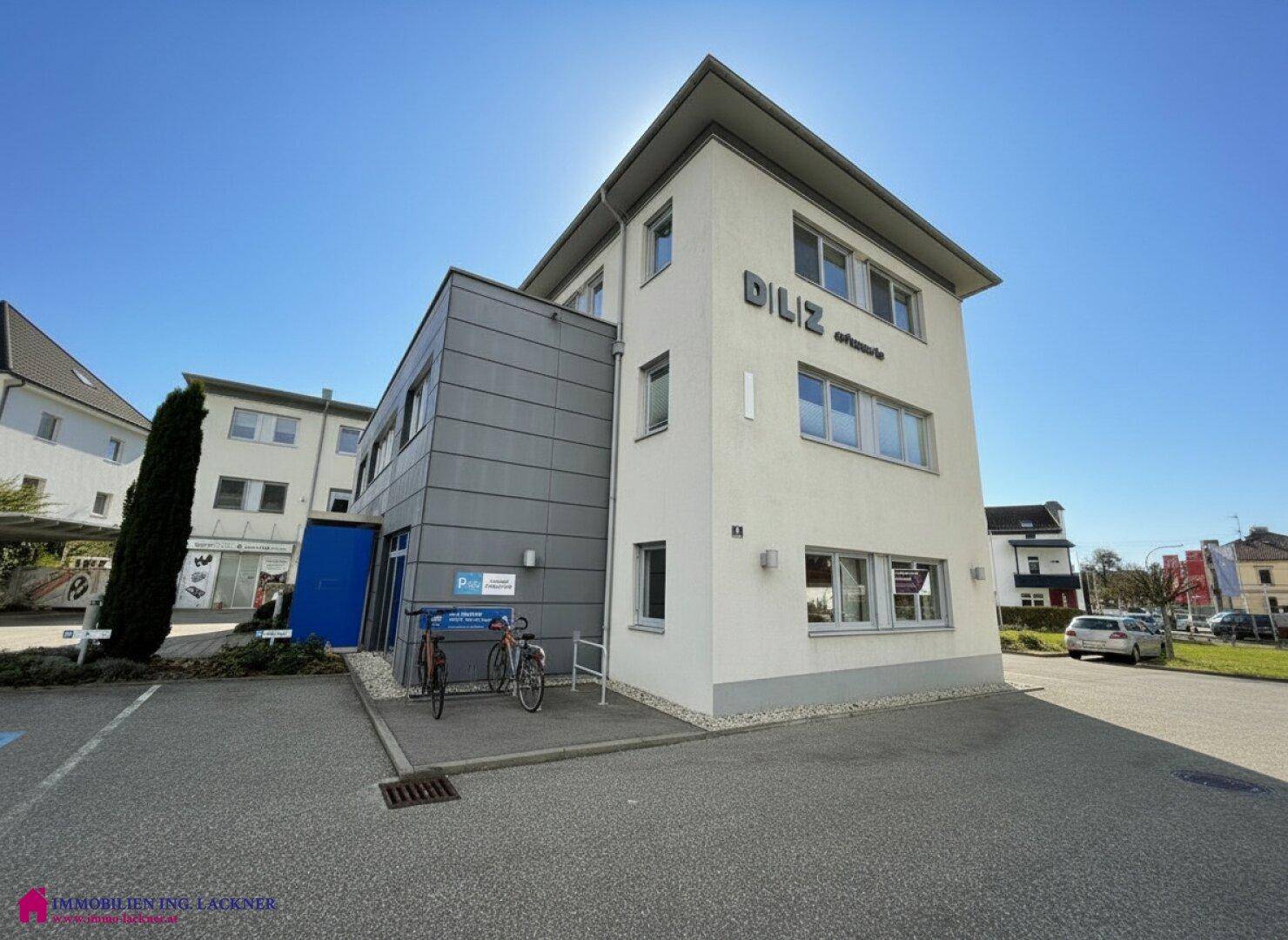 Modernes Geschäftsgebäude mit klaren Linien und Parkplätzen im Außenbereich unter blauem Himmel.