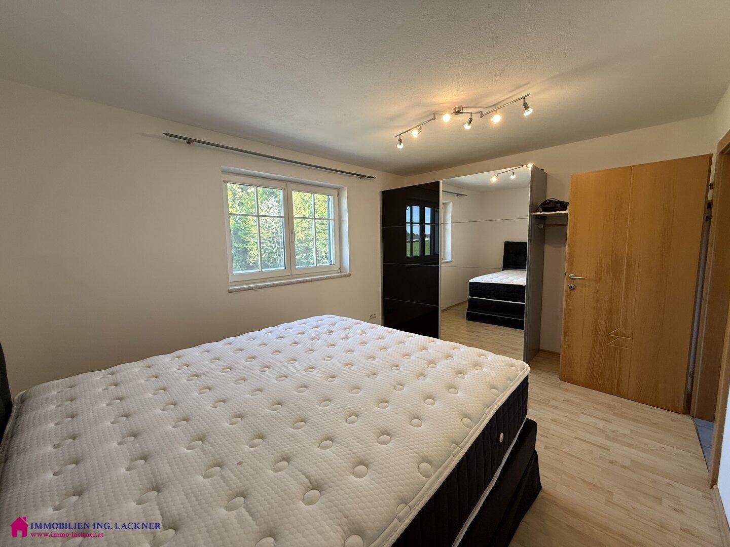 Schlafzimmer mit Doppelbett, hellem Laminatboden und Fenster mit Blick ins Grüne.