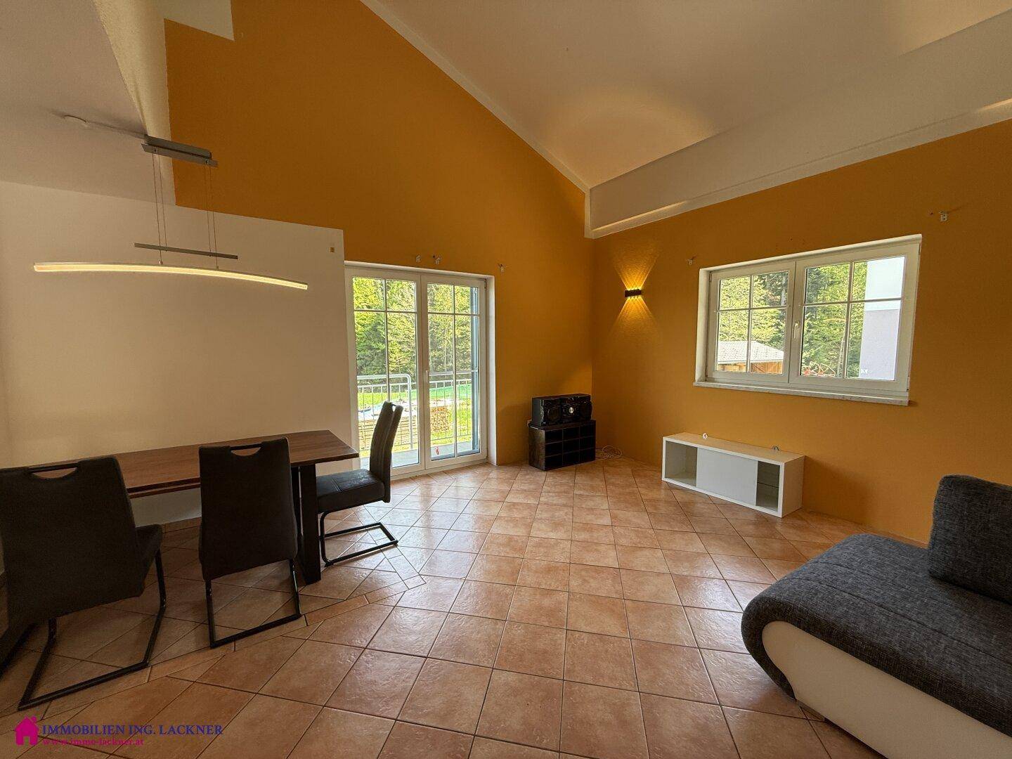 Geräumiges Wohnzimmer mit hohen Decken, gelben Wänden und Zugang zum Balkon.