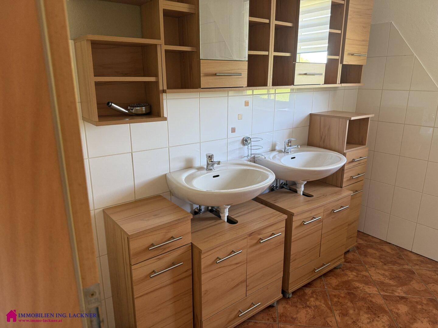 Badezimmer mit Doppelwaschbecken, Holzunterschränken und weißen Wandfliesen.