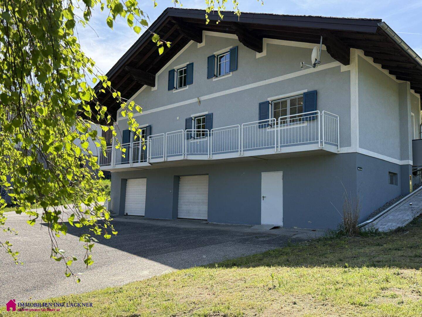 Traditionelles Haus mit Balkon und Garagen, umgeben von Bäumen und grüner Natur.