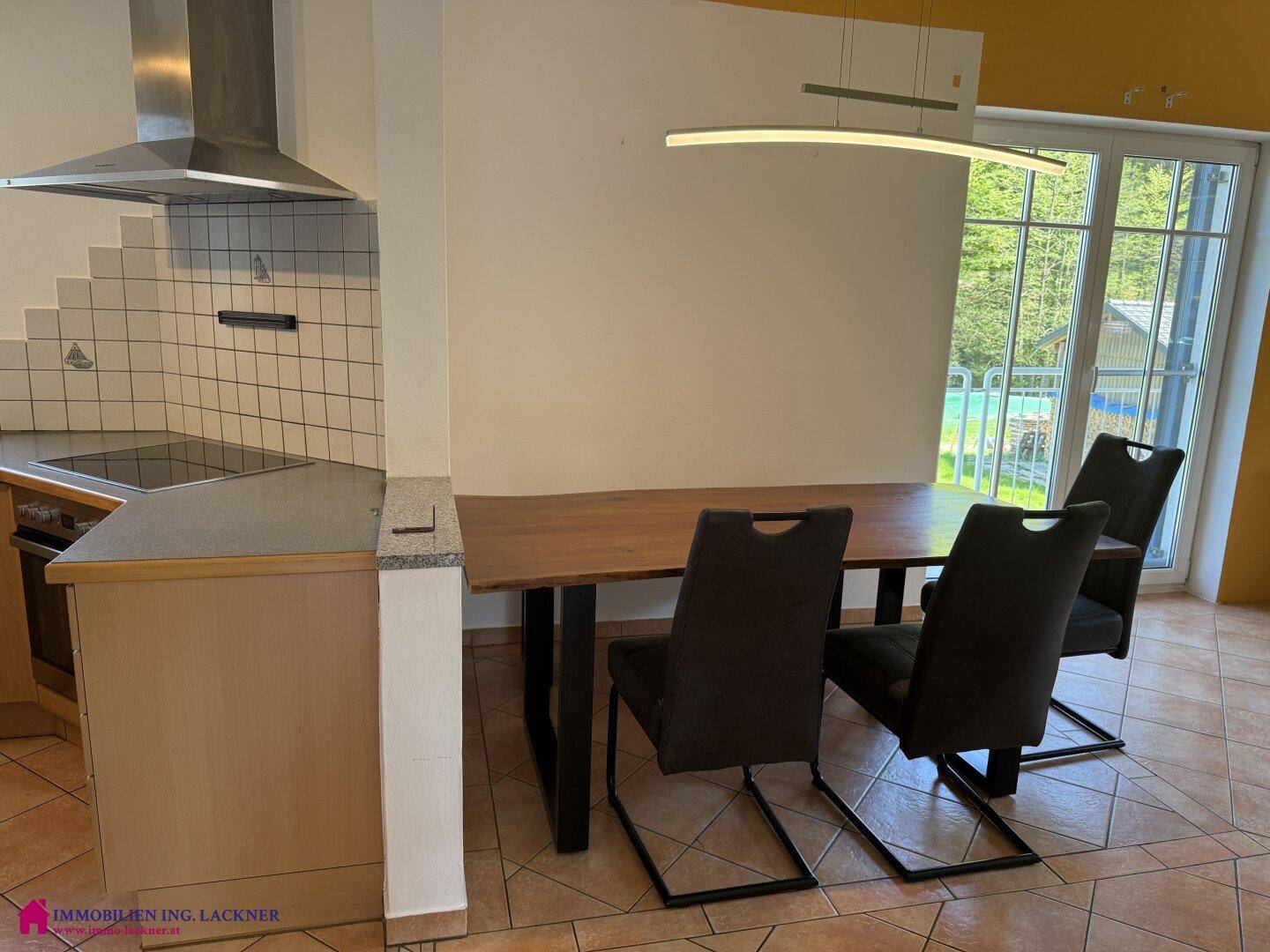 Offener Essbereich mit Holztisch und Blick auf die Küche und den Balkonzugang.