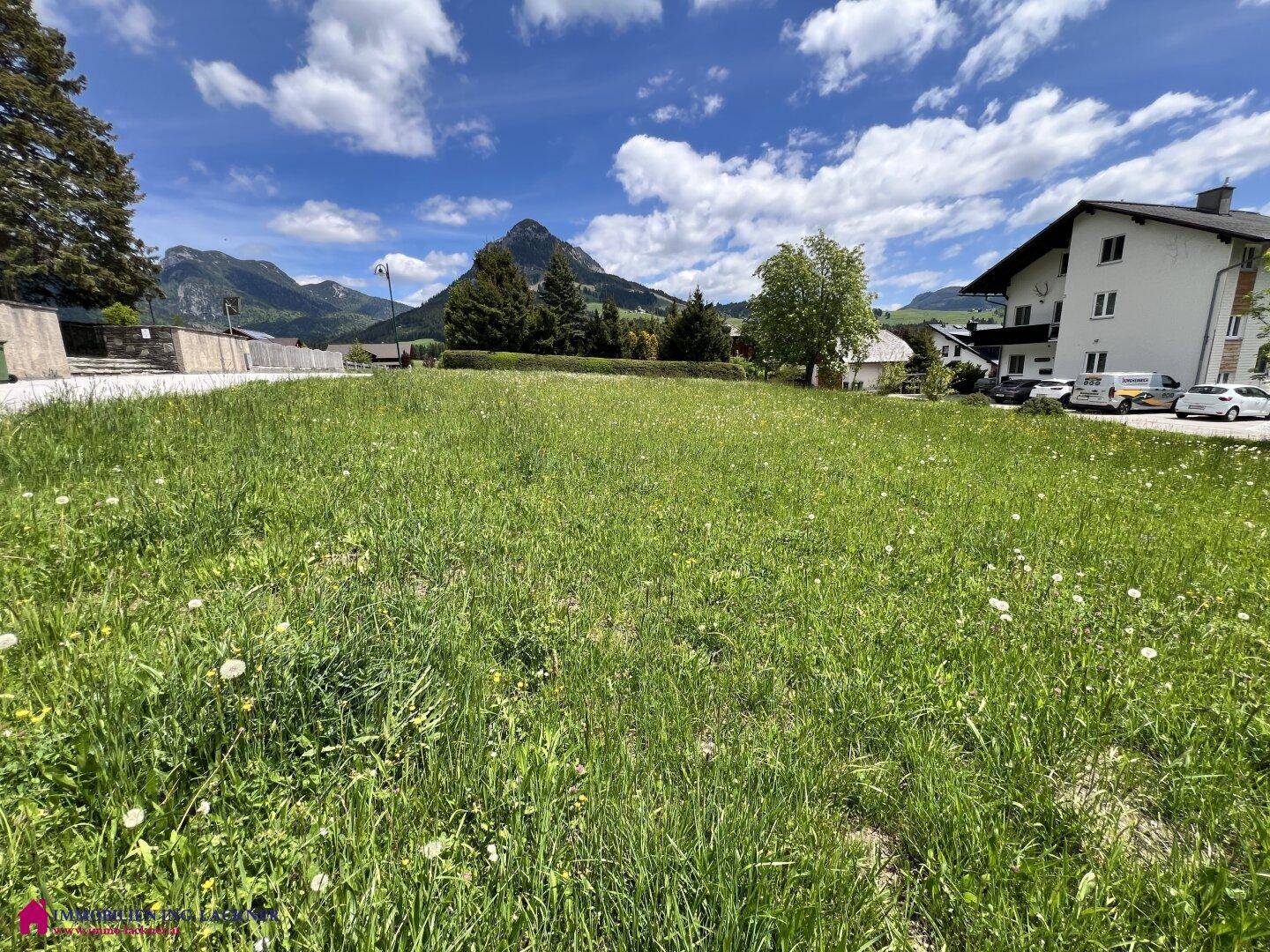 Sonnige Grünfläche mit Blick auf die umliegende Bebauung und die beeindruckende Bergkulisse.