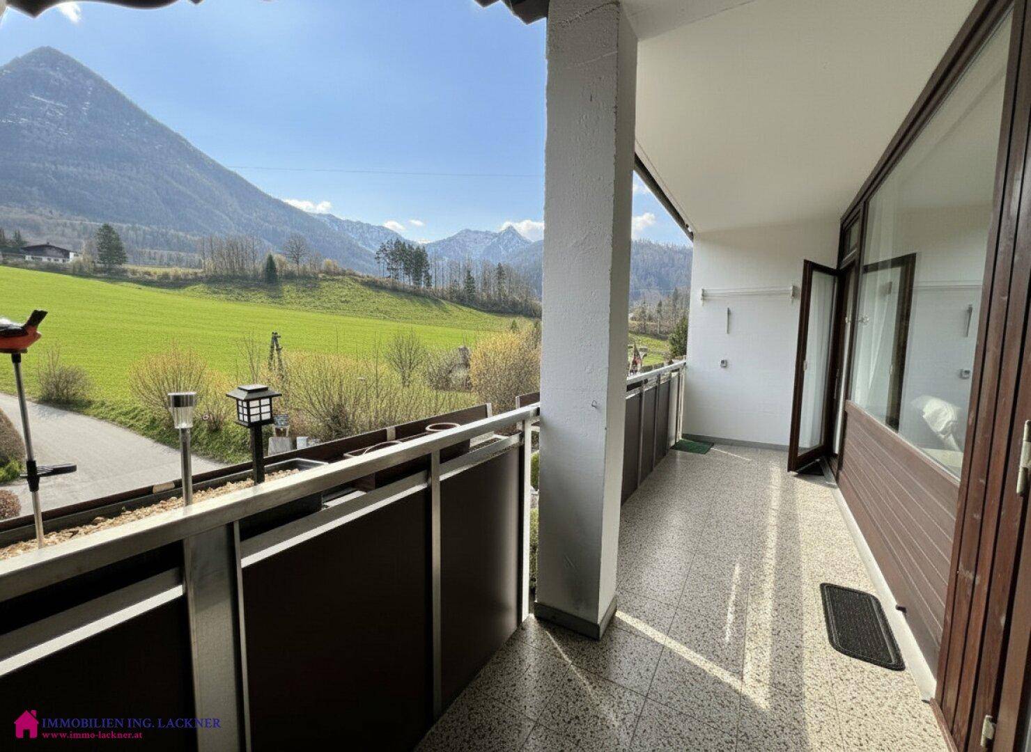 Sonniger Balkon mit Fliesenboden und Zugang zum Innenbereich, mit Panoramablick auf die Berge und Wiesen.