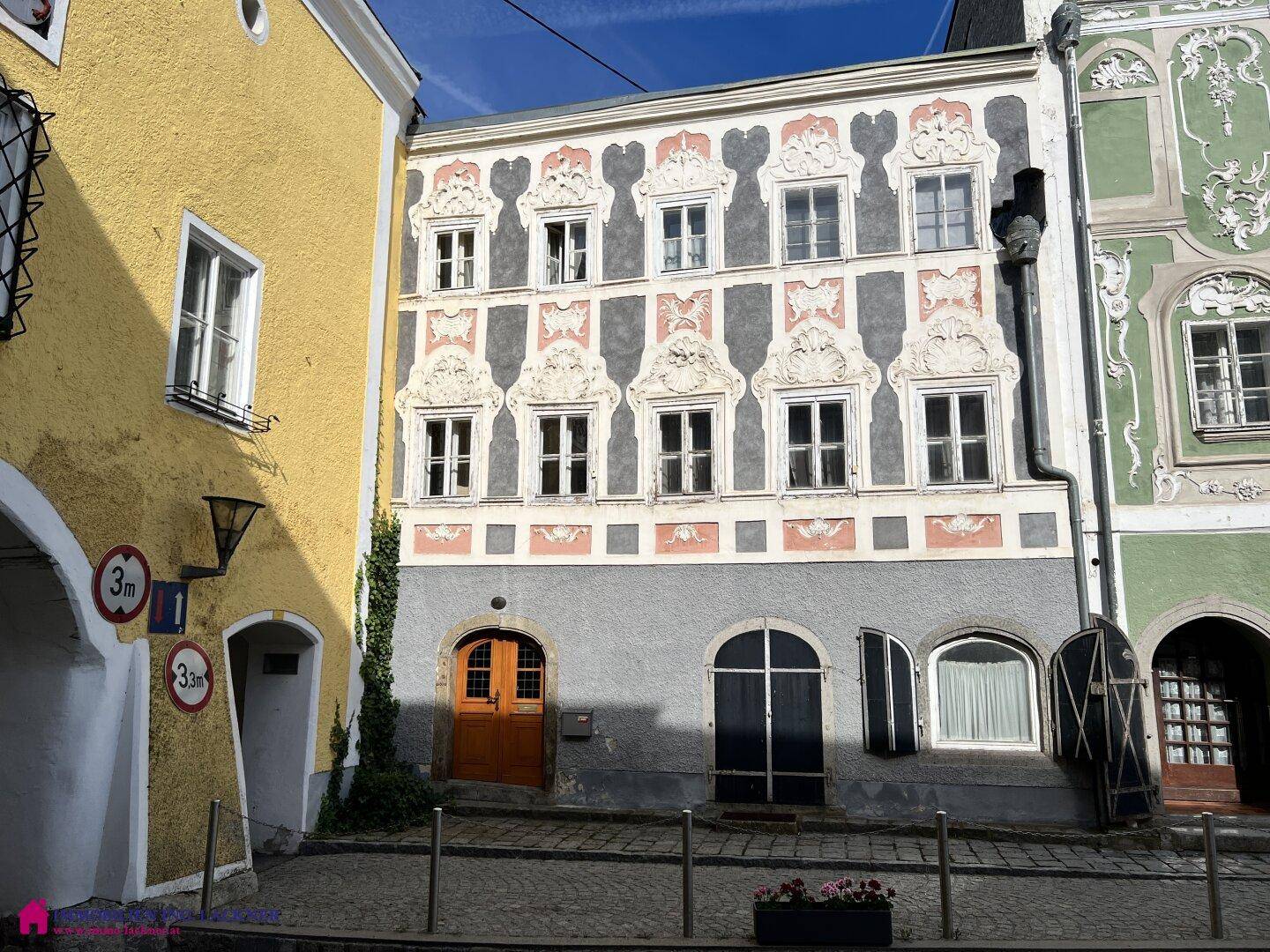 Historische Fassade eines Gebäudes mit kunstvollen Verzierungen und Fenstern in einer Altstadtgasse.