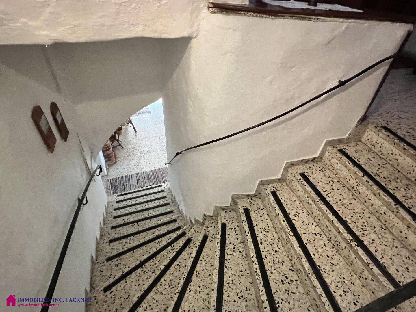 Geschwungene Steintreppe mit Terrazzostufen und schmiedeeisernem Geländer in einem historischen Gebäude.