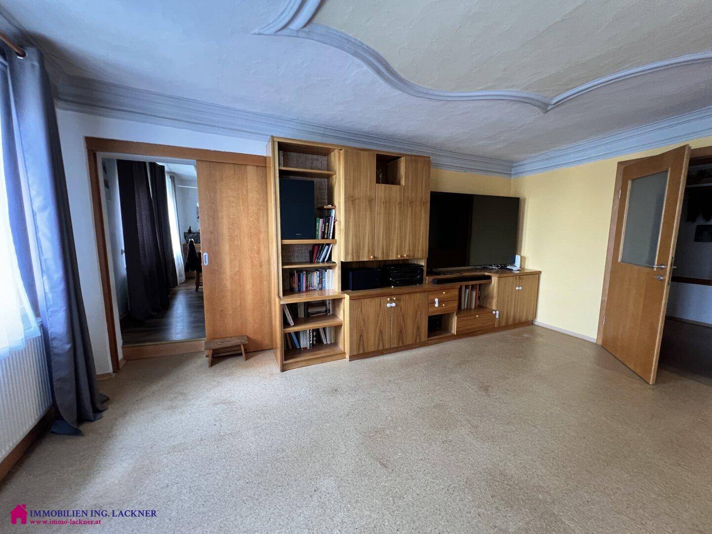 Wohnzimmer mit Teppichboden, Einbauschränken und einer dekorativen Stuckdecke.