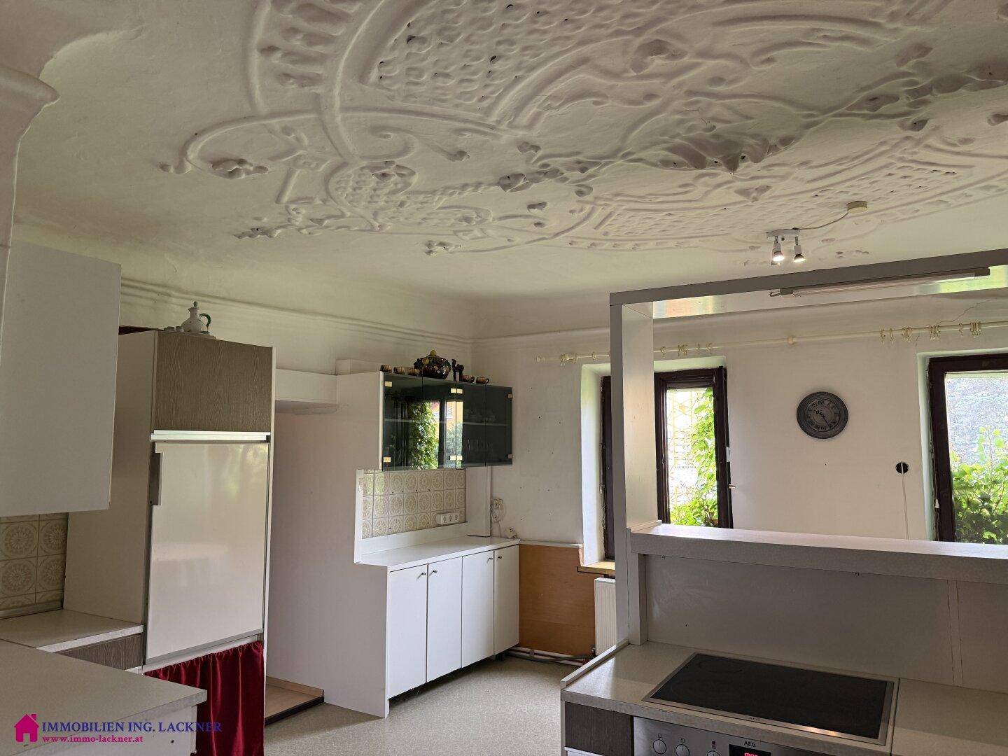 Küche mit Stuckdecke, weißen Schränken und Blick auf den begrünten Außenbereich.