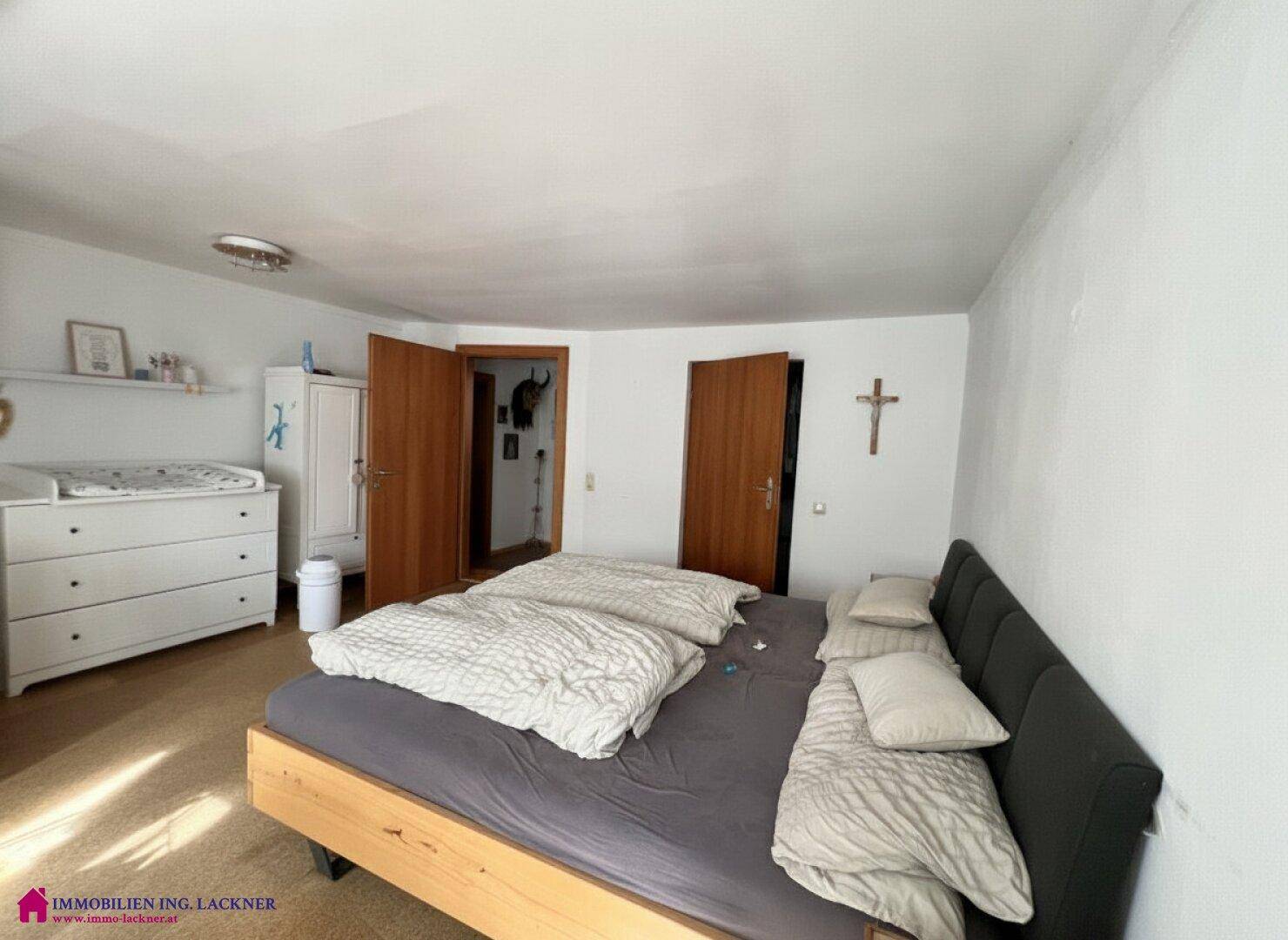 Schlafzimmer mit Doppelbett, hellem Teppichboden und schlichten weißen Wänden.
