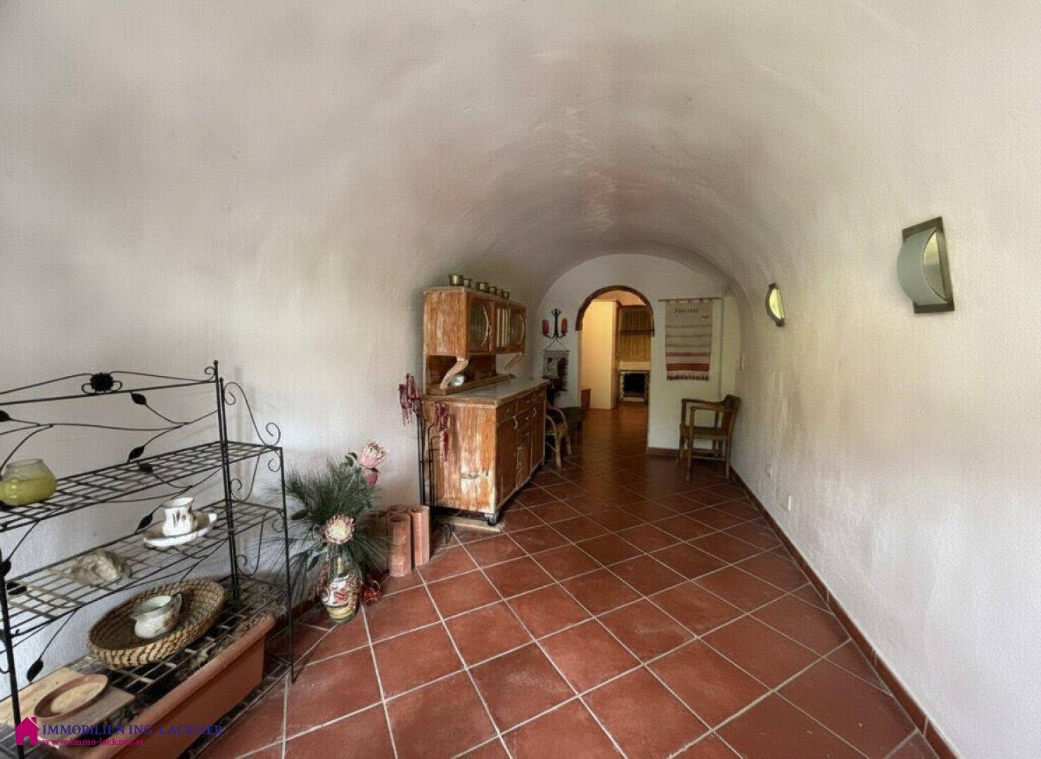 Langer Flur mit Terrakottafliesen, gewölbter Decke und rustikalen Holzmöbeln.