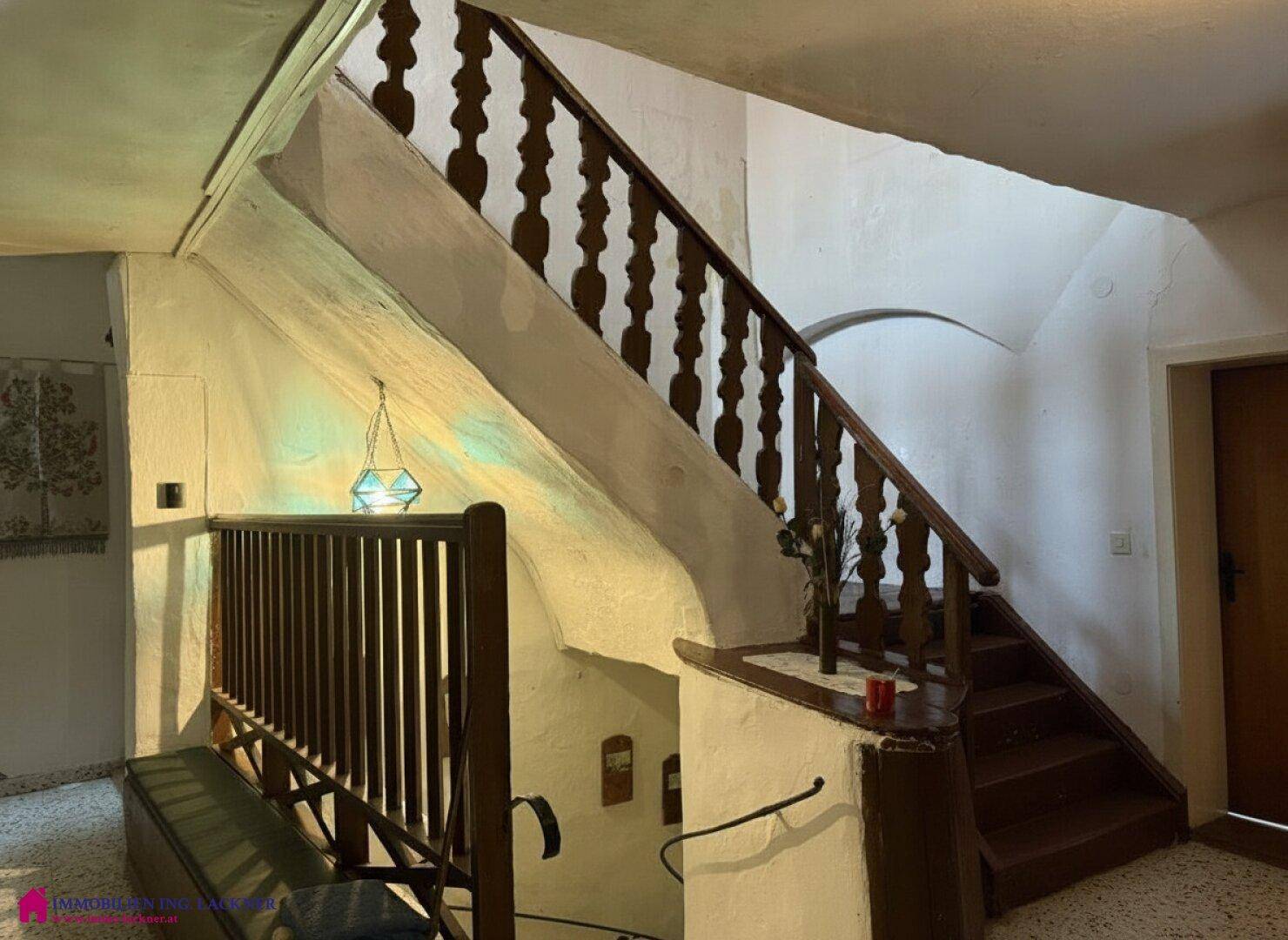 Holztreppe mit gedrechseltem Geländer und weiß getünchten Wänden in einem traditionellen Haus.