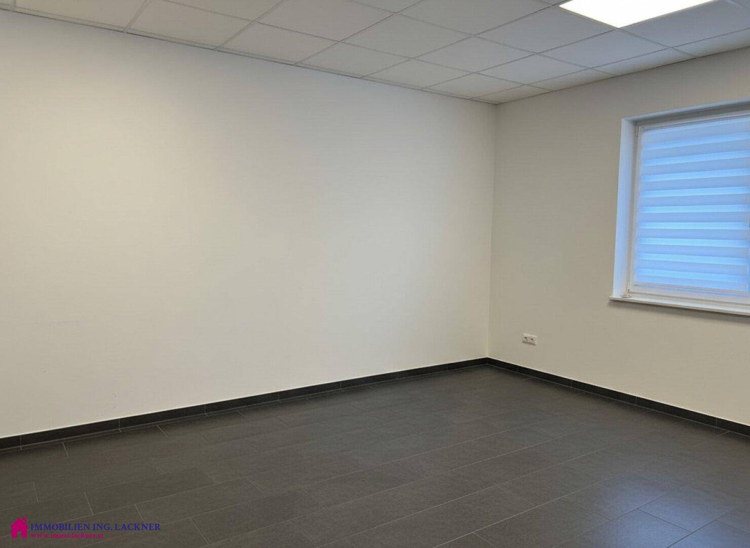 Helles, leeres Büro mit dunklem Fliesenboden und einem Fenster mit Jalousien für Privatsphäre.