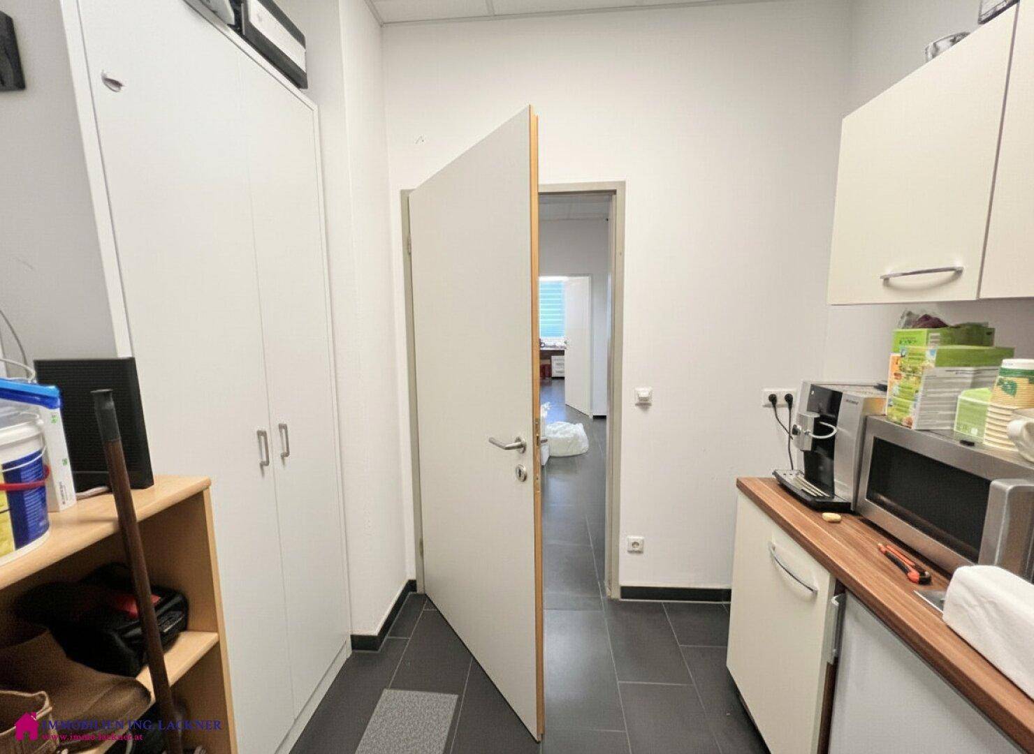 Funktionale Teeküche mit Holzarbeitsplatte, Mikrowelle und Kaffeemaschine, angrenzend an einen Bürobereich.