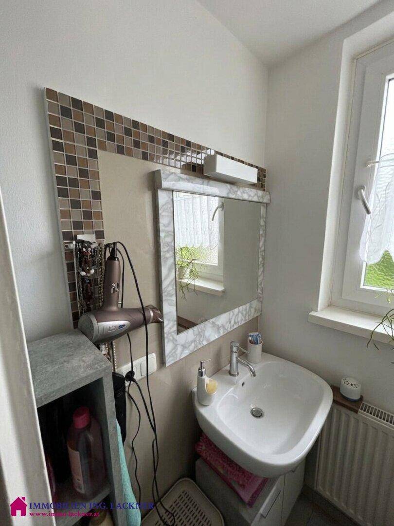 Detailansicht des Badezimmers mit Waschbecken, Spiegel und dekorativen Mosaikfliesen.
