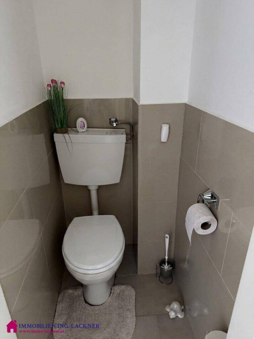 Separates WC mit Toilette und halbhoch gefliesten Wänden in neutralen Farbtönen.