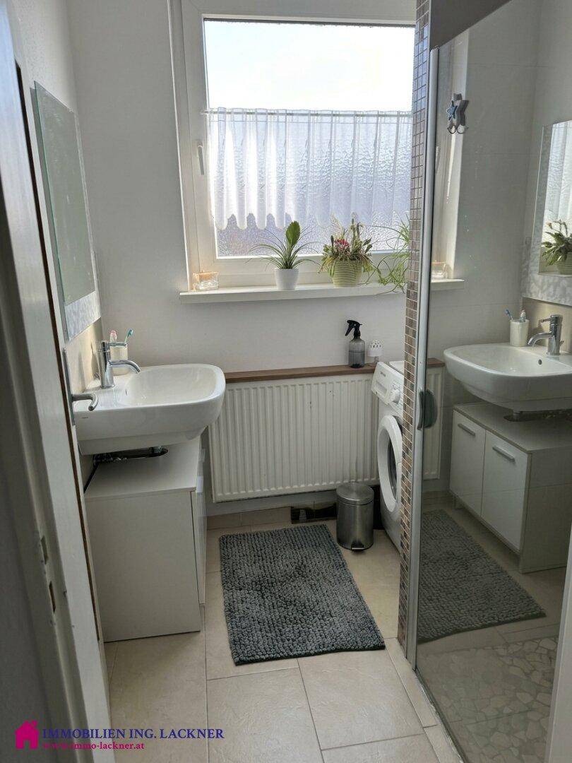Modernes Badezimmer mit Dusche, Waschbecken, Waschmaschine und Fenster für Tageslicht.