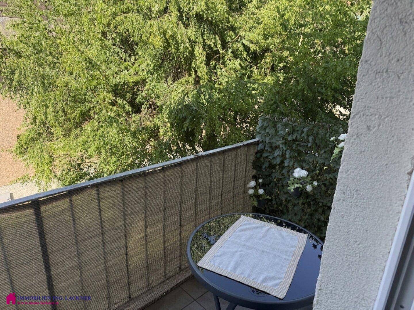 Nahaufnahme des Balkons mit einem kleinen Tisch und Blick auf üppiges Grün.