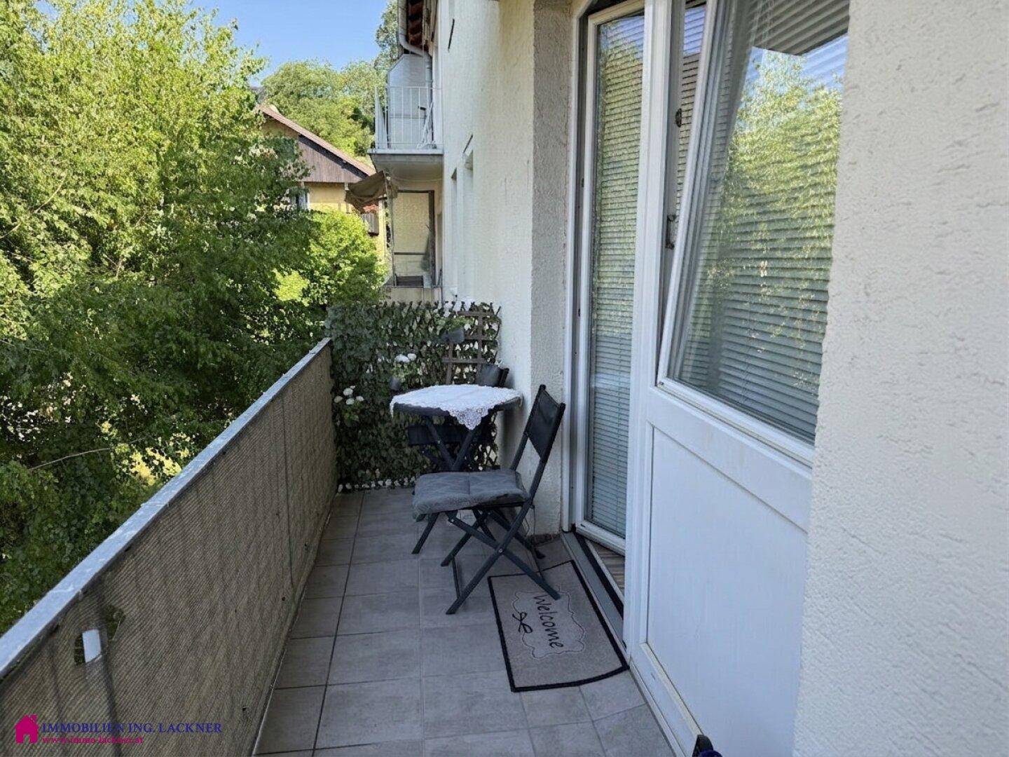 Gemütlicher Balkon mit Fliesenboden, kleinem Tisch und Stühlen, umgeben von viel Grün.