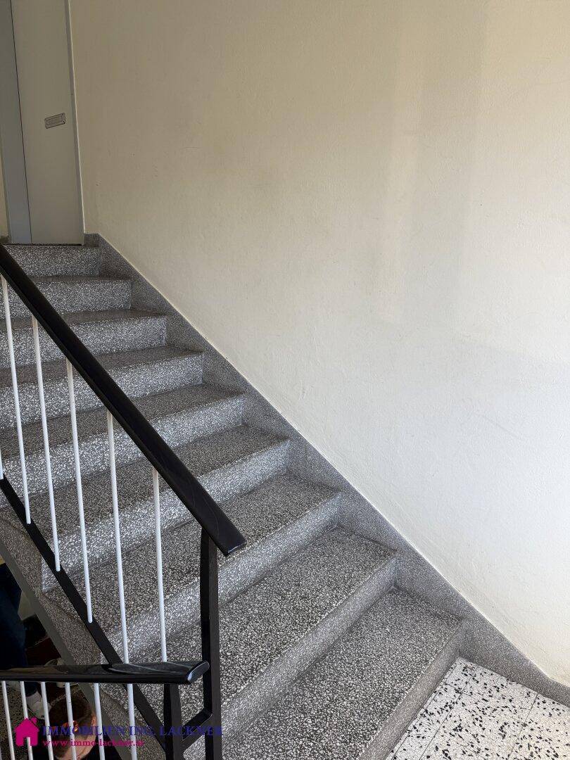 Treppenhaus mit Terrazzostufen und einem stabilen Metallgeländer in einem Mehrfamilienhaus.