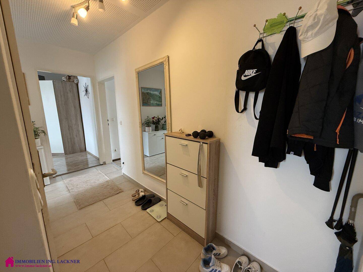 Eingangsbereich mit Fliesenboden, Spiegel und Garderobe, der zu den Wohnräumen führt.