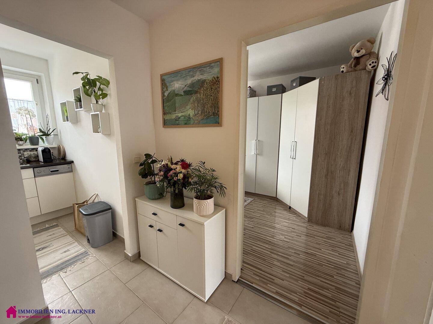 Heller Flur mit Fliesenboden, Schuhschrank und Zugang zur Küche und einem weiteren Zimmer.