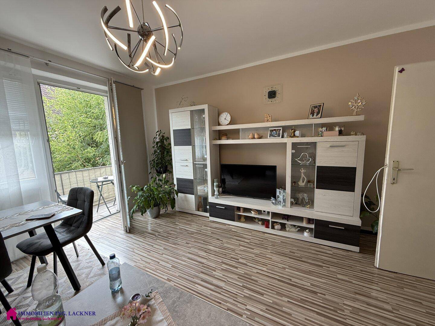 Wohnbereich mit TV-Möbeln, Essbereich und direktem Zugang zu einem kleinen Balkon.