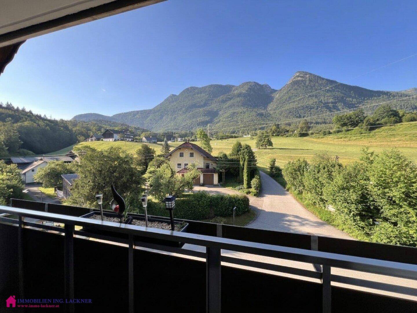 Panoramablick vom Balkon auf die umliegende Berglandschaft und grüne Felder an einem sonnigen Tag.