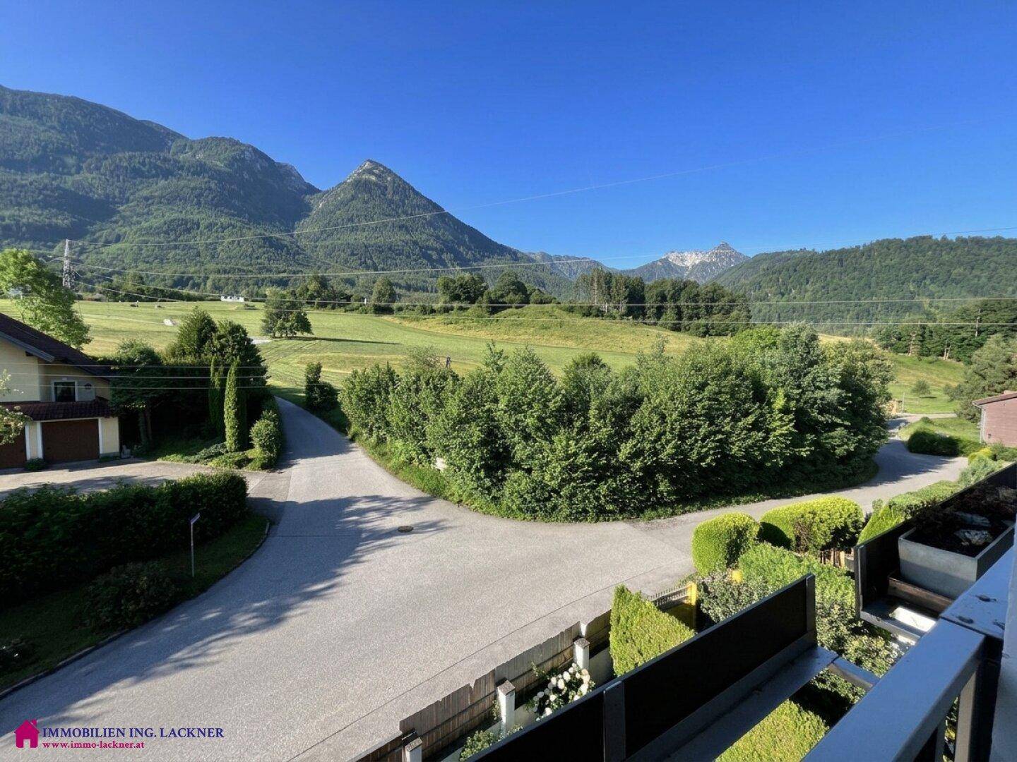 Weitläufiger Ausblick vom Balkon auf die grüne Landschaft und die majestätischen Berge.