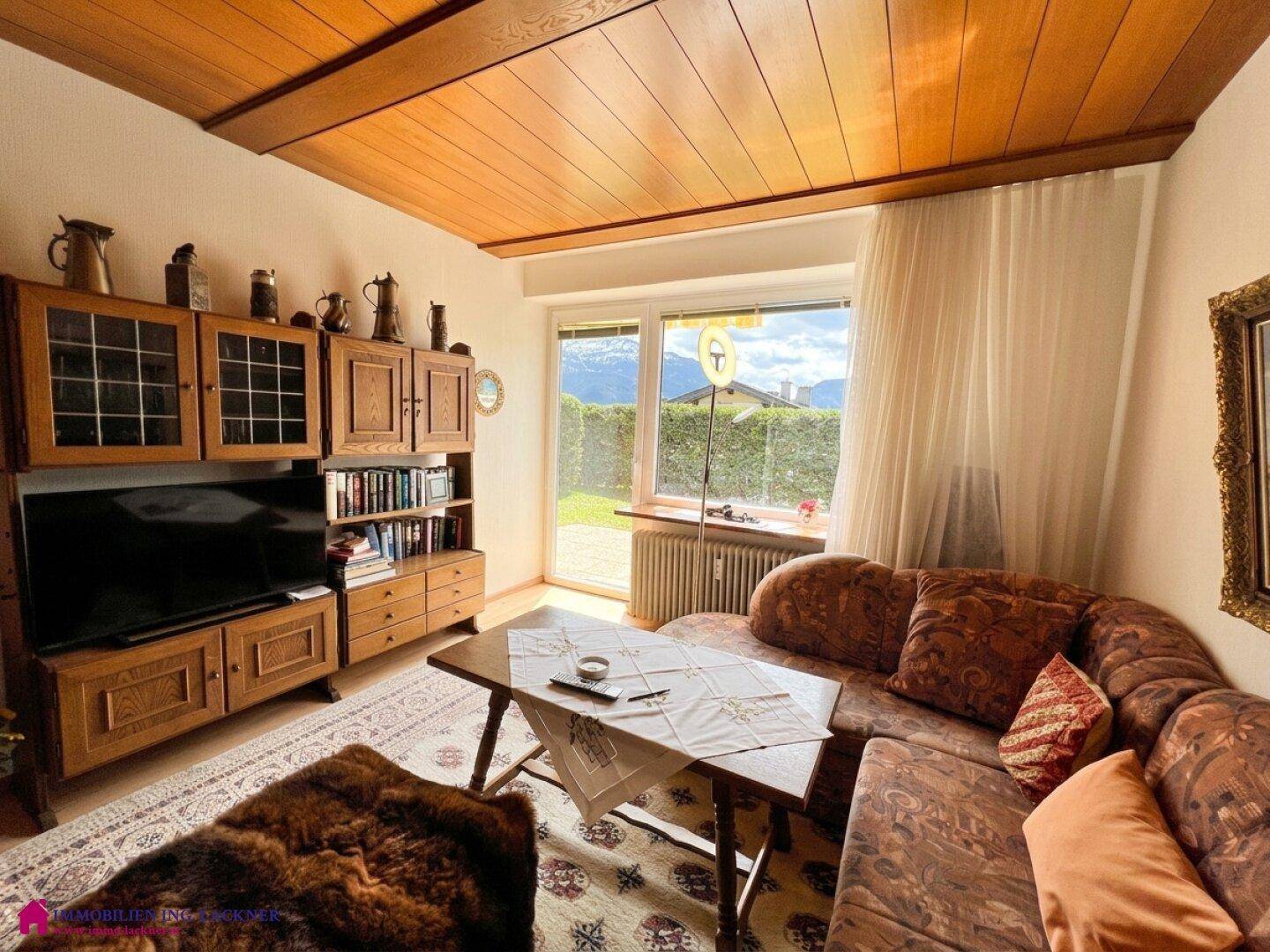 Helles Wohnzimmer mit Holzdecke, rustikalen Möbeln und weitem Blick auf die Berglandschaft.