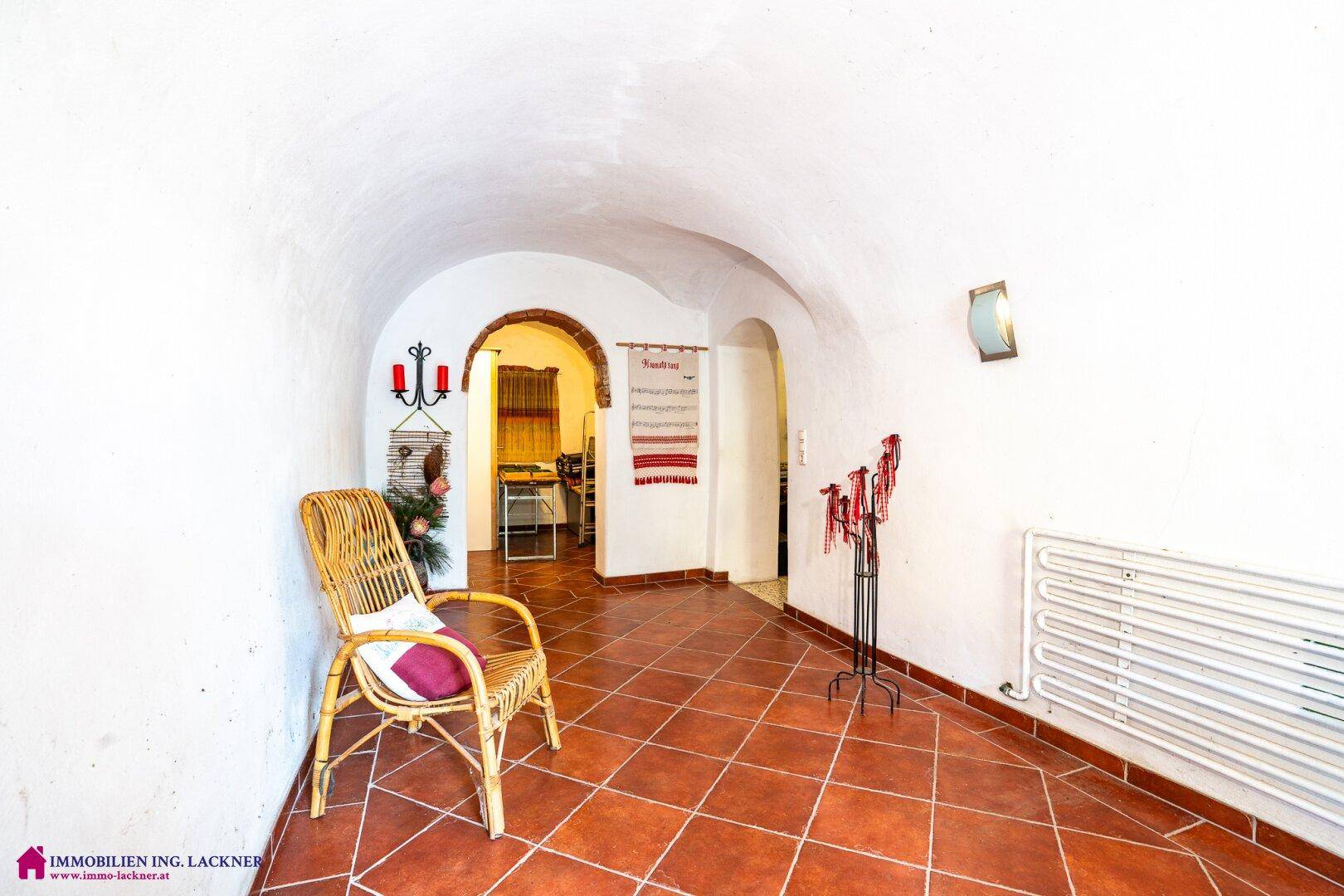 Gewölbter Flur mit Terrakottafliesen, Korbstuhl und traditionellen Wanddekorationen.