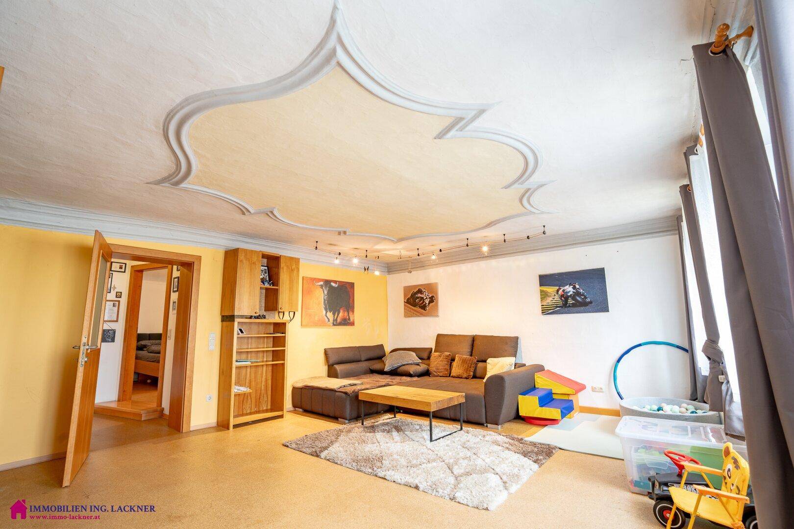 Modern eingerichtetes Wohnzimmer mit dekorativer Stuckdecke, Sofa und Teppich.
