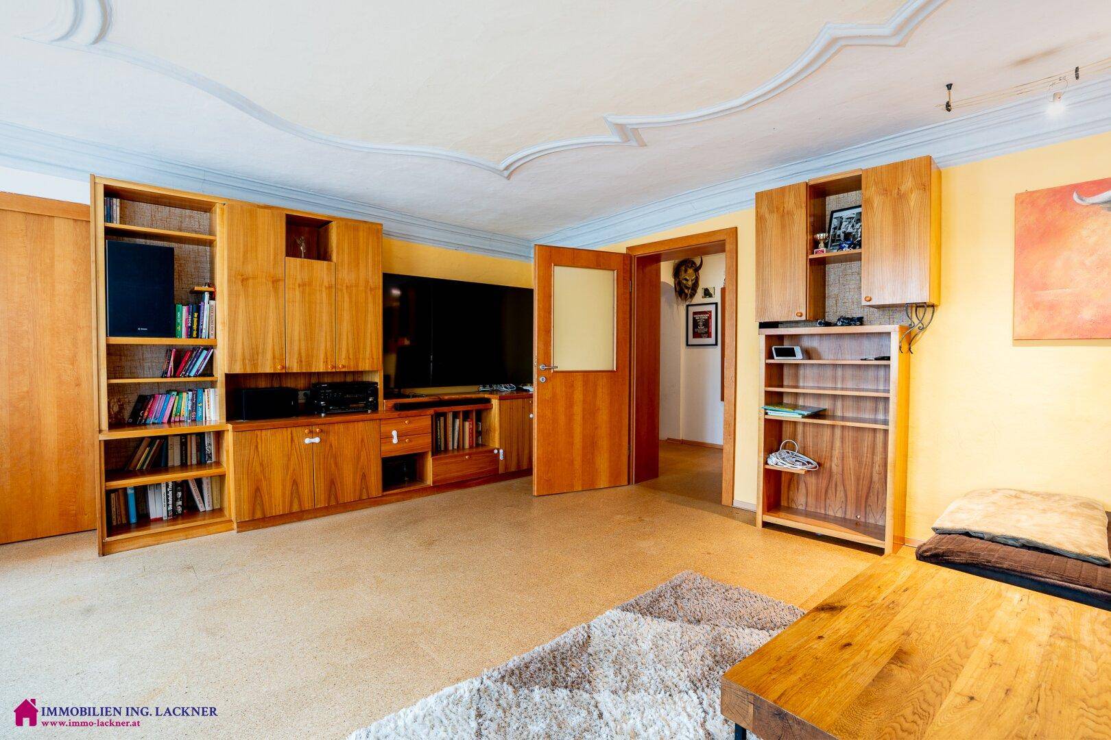Geräumiges Wohnzimmer mit Holzeinbauten, Stuckdecke und einem großen Fernseher.